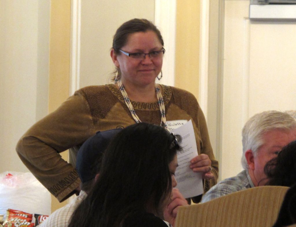 A woman wearing a name tag and holding a sheet of paper standing next to seated workshop participants