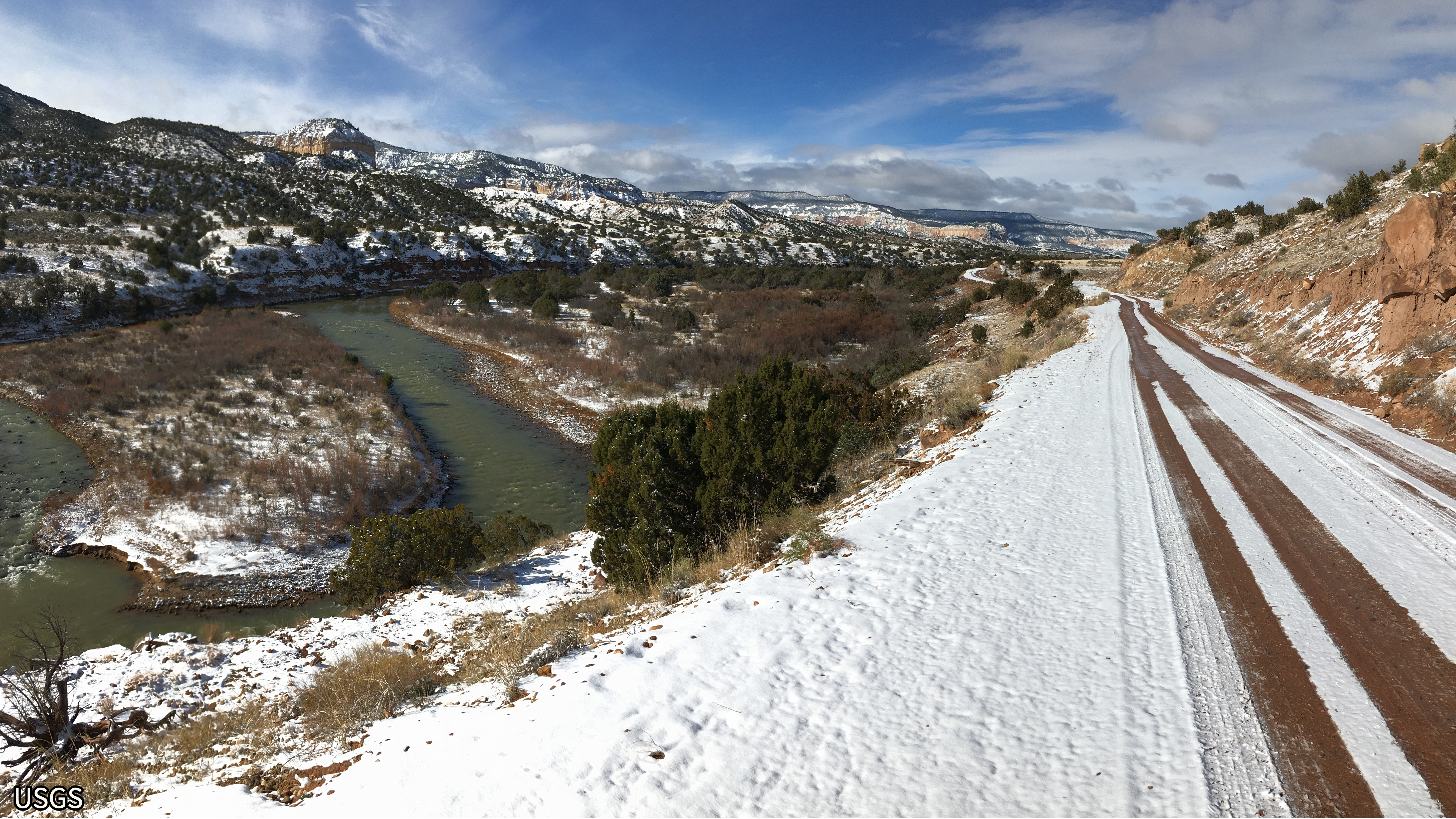 New Mexico mountains with snow and shrubs on them near a river. Snow covered road on right side.