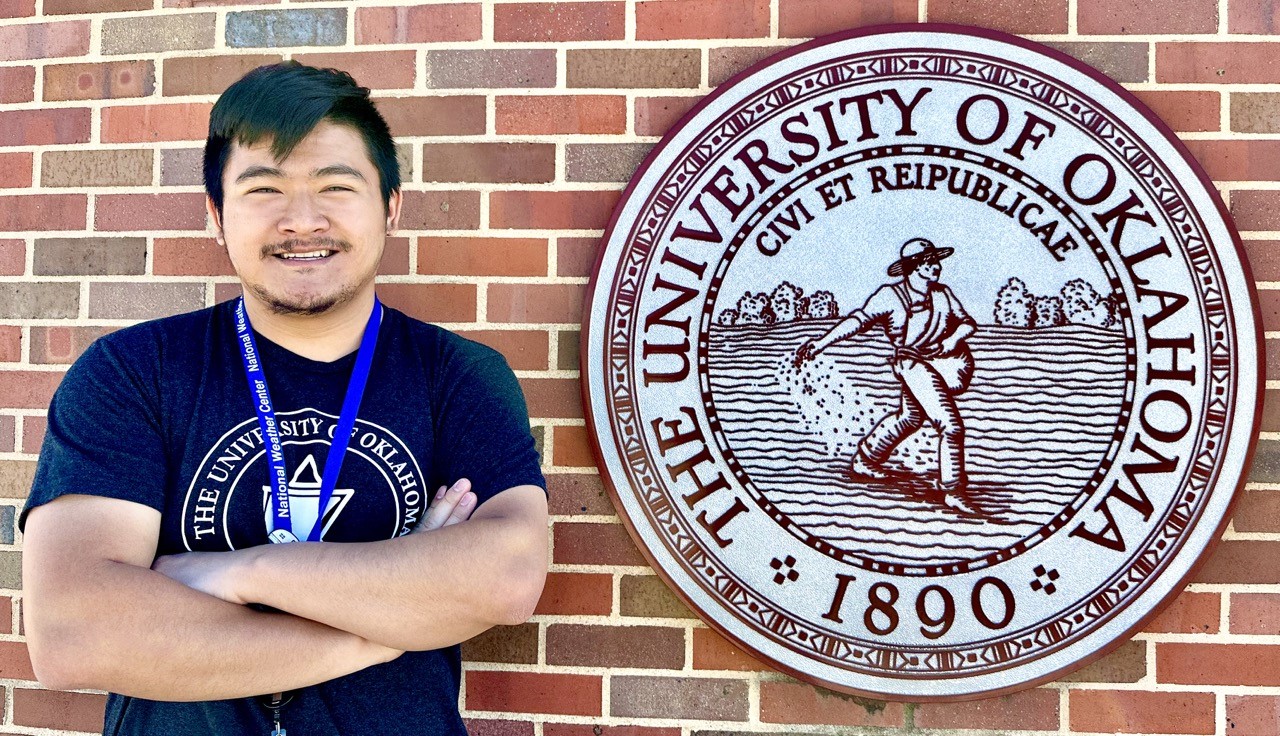 Liam Thompson poses next to the seal of The University of Oklahoma