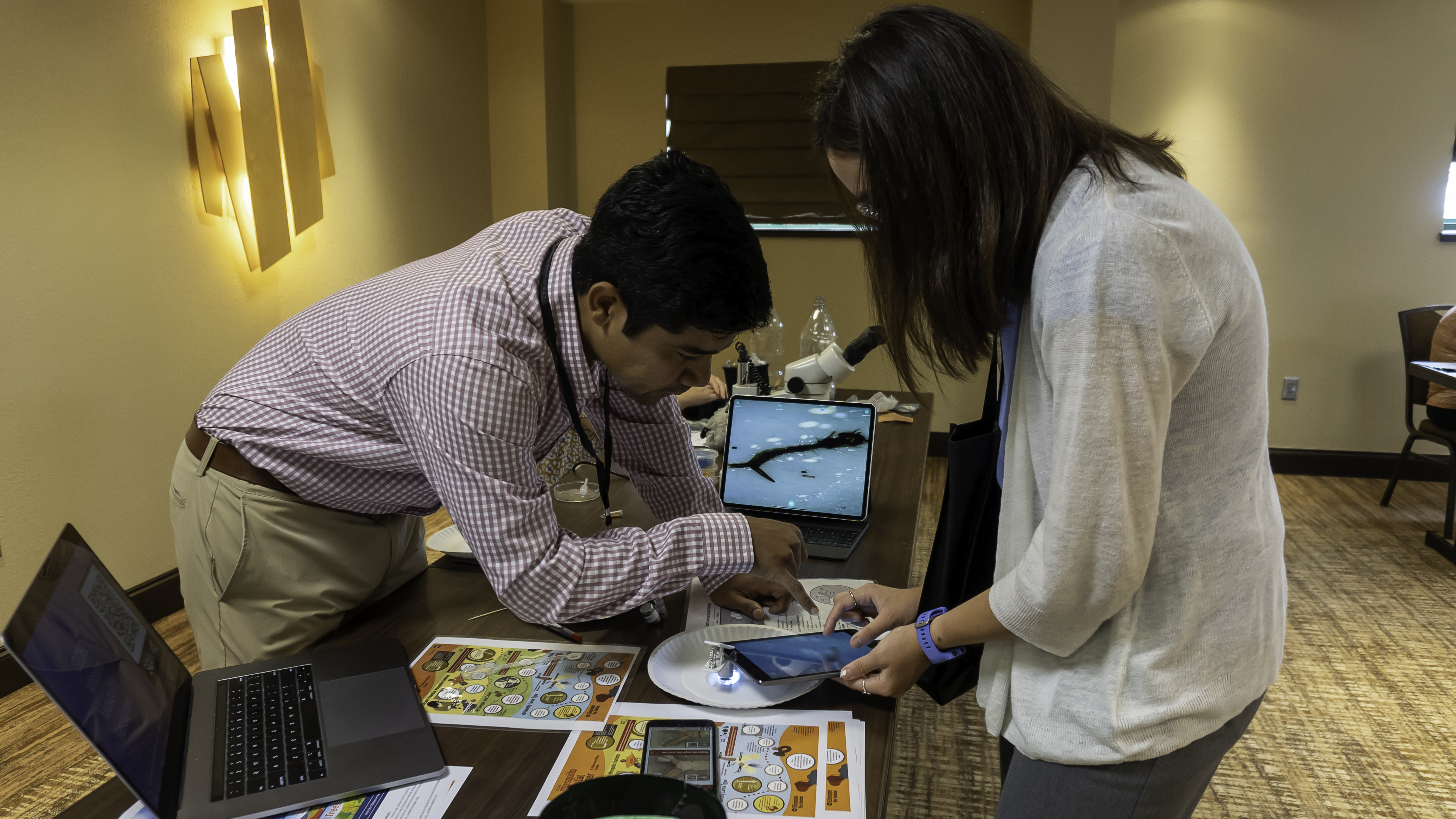 Two people look at a tablet screen at a magnified mosquito larva.