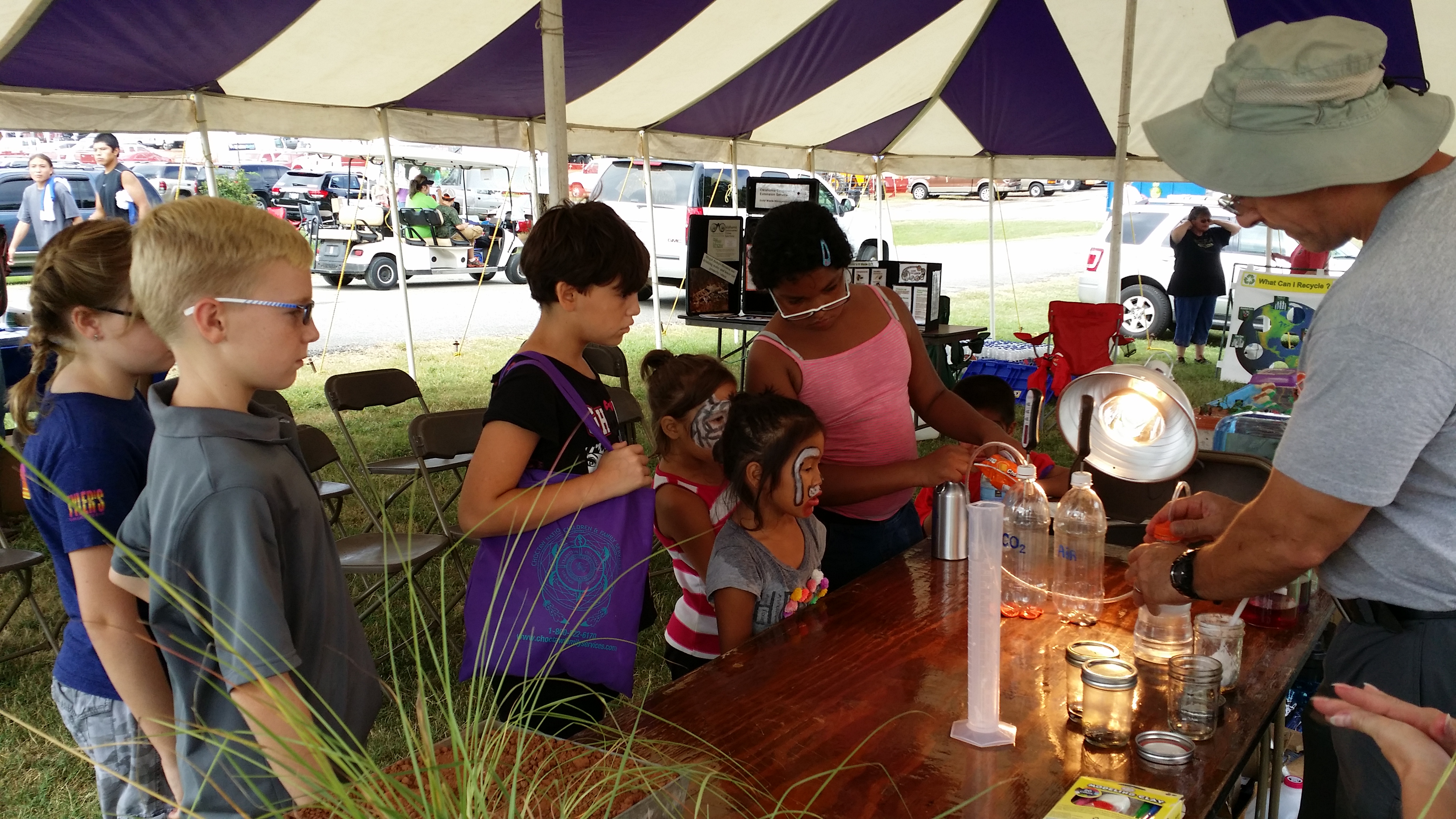 A group of children watch a demonstration of the activity under a tent