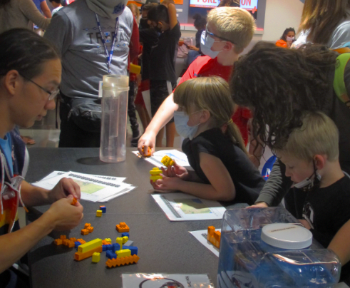 A group of children play with plastic blocks to model this activity