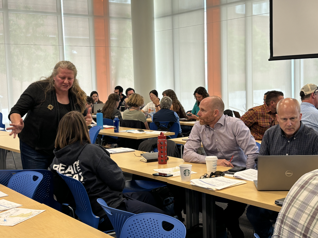 One person standing next to a couple of sitting people talking during the workshop